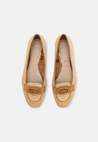 Mocassins en textile tissé beige avec une sangle en cuir tan ornée d'une touche de matériel doré. Doublure intérieure douce avec semelle rembourrée.
