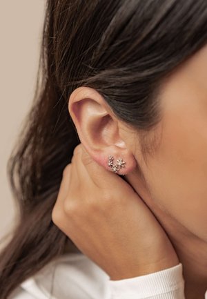 Nahaufnahme eines Ohrs einer Frau mit dunklem Haar, die zarte silberne Blumenohrringe trägt und ihre Hand sanft in der Nähe ihres Halses hält.