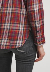 Camicia a scacchi rossa e blu con maniche lunghe e polsini abbottonati. Indossata con jeans grigio scuro che presentano un dettaglio tasca consumato.