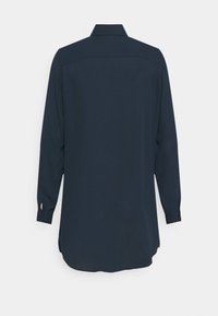 Chemise bleu marine foncé à manches longues avec col, poignets boutonnés et ourlet arrondi, vue de dos sur un fond uni.