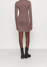 Rippkleid in Lavendel mit langen Ärmeln und figurbetonter Silhouette. Getragen mit schwarzen Stiefeletten. Glatte Textur und Midi-Länge.