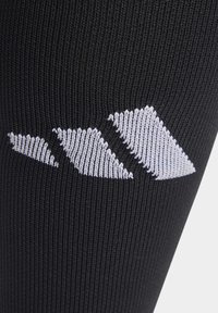 Chaussette de sport noire avec un tissu texturé et un motif géométrique blanc près du haut, offrant un contraste avec le fond sombre.