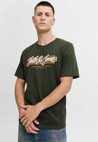 Groene katoenen T-shirt met korte mouwen en een ronde hals. Bevat een witte en oranje grafische print met tekst op de voorkant.