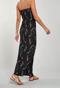 Czarna sukienka bez ramiączek z kwiatowym wzorem, dopasowanym gorsetem i zwiewnym krojem. Płaskie brązowe sandały dopełniają stylizację.