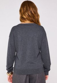 Pull en maille gris foncé avec une coupe décontractée, un large col et des manches longues. Ourlet et poignets côtelés ; texture lisse avec un minimum de détails.