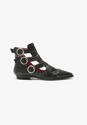 Stivaletto alla caviglia in pelle nera con punta appuntita, ritagli, tre cinturini decorativi con fibbie circolari e borchie metalliche. Foderato internamente con un vivace rivestimento rosso.
