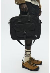 Borsa per laptop in nylon nero con due manici superiori, chiusura con zip, tasca frontale e dettaglio con logo. Dotata di tracolla regolabile e design elegante.