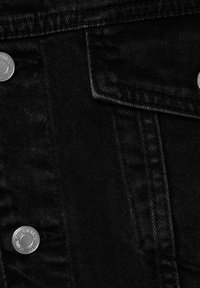 Gros plan sur un tissu en denim noir avec des boutons en métal argenté et une poche à rabat cousue.