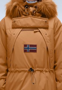 Orange parka med et faux fur hætte, justerbar snoreliv, frontlynlås lomme og et norsk flag patch på brystet.