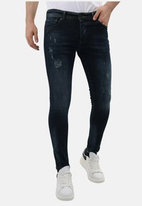 Donkerblauwe denim jeans met verwerkte details, met een slim fit en een gematigde stretch. Gecombineerd met witte sneakers voor contrast.