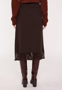 Gonna di tessuto marrone intrecciato con orlo a frange, due tasche posteriori, abbinata a stivali borgogna al ginocchio. Tessuto strutturato, lunghezza a metà polpaccio.