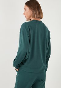 Felpa verde con vestibilità relax, spalle scese e polsini a coste. Texture morbida con una finitura liscia e opaca, dal design semplice.