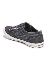 Sneaker nera in tela con cuciture bianche, profilo basso, punta rotonda e suola in gomma bianca con il marchio "CREEKS" sul tallone.