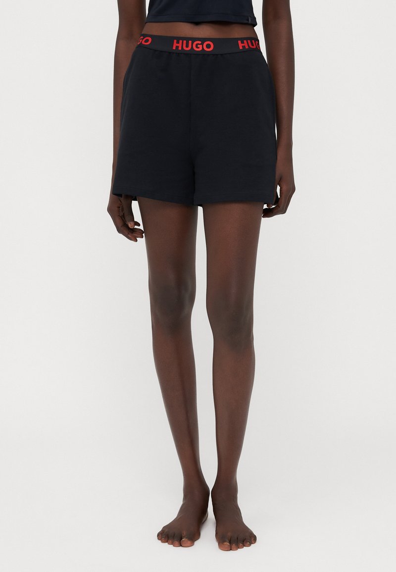 Svarta bomullsshorts med ett rött "HUGO"-logoband i midjan, har en avslappnad passform och en slät textur.