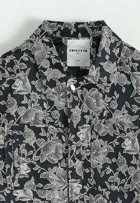 Chemise noire à motif floral, avec un motif de fleurs grises délicat, tissu à la texture douce, col pointu et poche plaquée sur le devant.