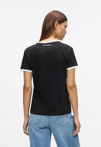 T-shirt preto de manga curta com colarinho e bainhas brancas. Apresenta um logótipo nas costas. Material de algodão macio, corte clássico, design limpo.