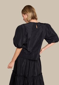 Svart topp med pufferm som er laget av skinnende stoff, med en nøkkelhull-design bak og en avslappet passform, kombinert med et lagdelt skjørt.