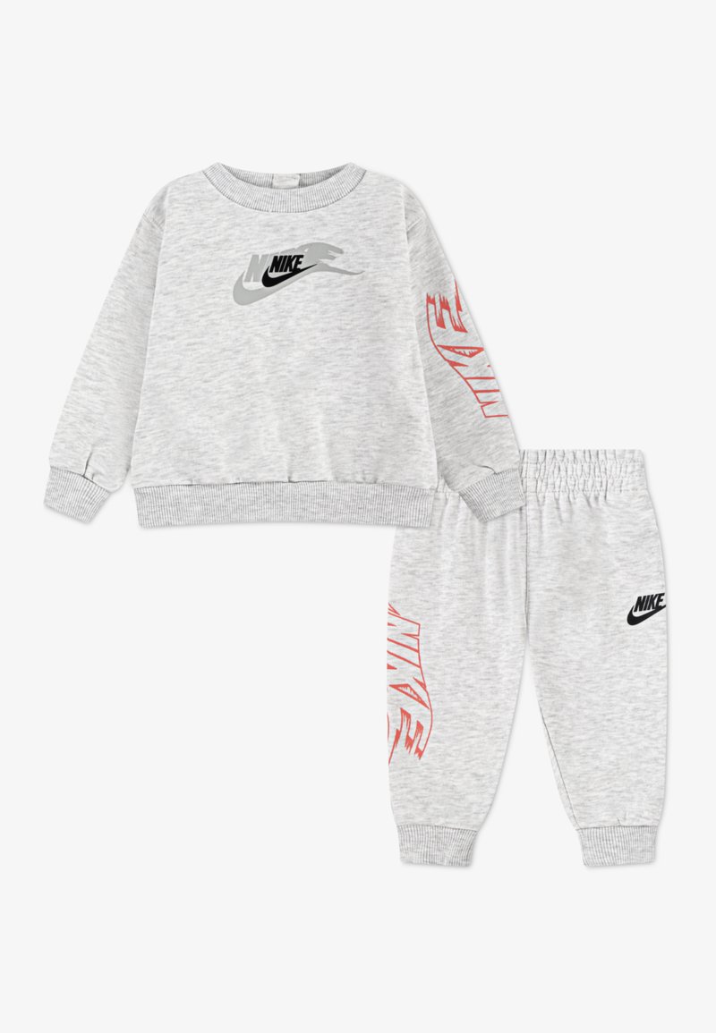 Graues Sweatshirt- und Hosen-Set aus weichem Stoff. Das Sweatshirt hat ein schwarzes und graues Nike-Logo; die Hose zeigt ein schwarzes Nike-Logo und rote Akzente.
