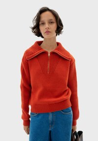 Czerwony sweter z dzianiny z wysokim kołnierzem, półzapięciem z przodu, ribbedman żebrowanymi mankietami oraz wzorem teksturowym na kołnierzu i korpusie.