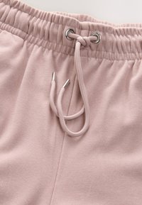 Soft pink sweatpants with an elastic waistband, featuring a drawstring with metal tips and ribbed texture throughout.