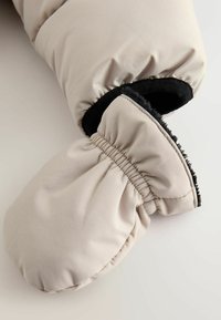 Hellbeige gepolsterte Handschuh mit elastischem Handgelenk, schwarzer Innenfutter und glatter Außentextur. Abgerundete Form mit Raffung am Handgelenk.
