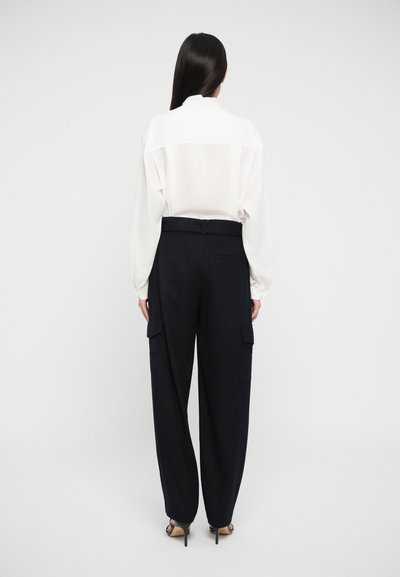 White long-sleeve blouse with a high collar paired with loose-fitting black cargo pants featuring side pockets and a smooth texture.