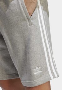 Shorts din bumbac gri, cu dungi albe accentuate, buzunare laterale și un logo brodat pe tiv. Textură moale și design casual.