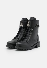Schwarze Lederstiefeletten mit runder Zehenform, Schnürung vorne und dekorativer silberner Hardware an einem Knöchelriemen. Texturiertes Gummisohle.