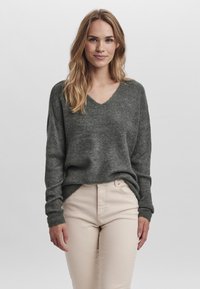 Pull en tricot côtelé gris avec un col en V et des manches longues, associé à un pantalon taille haute beige clair. Texture douce avec une coupe décontractée.