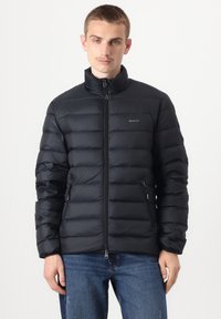 Schwarze Steppjacke mit durchgehendem Reißverschluss, hohem Kragen und zwei Seitentaschen. Verfügt über ein gestepptes Design und ein dezentes Logo auf der Brust.