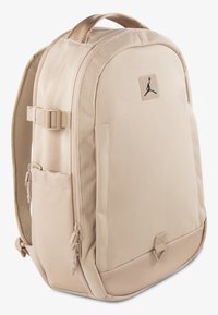 Beige hátizsák sima szövetfelülettel, cipzáras rekeszekkel, oldalsó hálós zsebekkel és fekete logóval az elején.