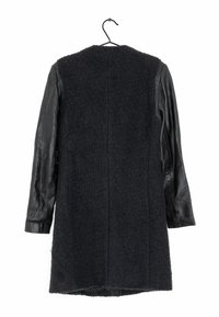 Abrigo negro con cuerpo de lana texturizada y mangas de cuero. Presenta un diseño sencillo, mangas largas y un dobladillo recto. Está colgado de un gancho.