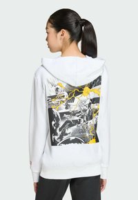 Sweat à capuche blanc avec un imprimé graphique au dos représentant des illustrations en noir et jaune de personnages et d’éclairs. Tissu doux, manches longues.