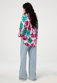 Floral print shirt with vibrant pink and teal flowers on a light background, paired with light blue wide-leg jeans, seen from the back.