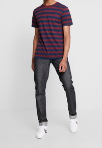 T-shirt à col rond rayé rouge et bleu marine, manches courtes, associée à un jean foncé et des baskets blanches. Tissu en coton avec une texture lisse.