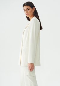 Witte blazer met een getailleerde pasvorm, voorzien van twee voorzakken en een gladde textuur. Het ontwerp heeft een geknipte revers en een open voorkant.