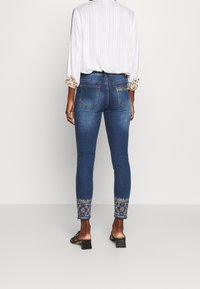 Hubené džíny v tmavě modrém denimovém provedení s vyšívanými květinovými detaily na manžetách. Mají design s pěti kapsami a středně vysokým pasem.