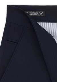 Granatowy materiał o teksturowanym wykończeniu, z metką „USZYTY NA MIARĘ” i paskowym wnętrzem. Widoczne szczegóły szwów.