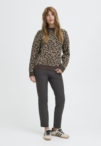 Pulover cu imprimeu leopard maro, cu guler rotund, combinat cu pantaloni slim-fit gri închis și adidași bej cu dungi negre.