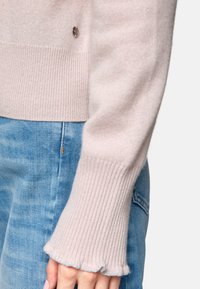 Helle rosa gestrickte Sweater mit gerippten Bündchen und einem zarten Rüschensaum, kombiniert mit hellblauer Jeans für einen lässigen Look.