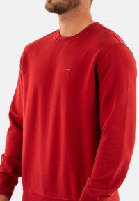 Sudadera roja tipo crewneck hecha de tejido suave. Cuenta con mangas largas y un pequeño logo blanco de Levi's en el lado izquierdo del pecho. Textura suave.
