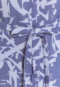 Paars jurkstof met abstracte, lichtgrijze tekstachtige patronen, voorzien van knopen en een ceintuur om de taille mee te accentueren.