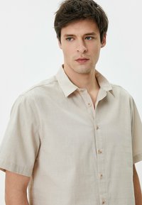 Licht beige short-sleeve overhemde met knoopjes, gemaakt van textuurstof, met een klassieke kraag en vijf bruine knopen aan de voorkant.