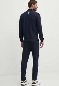 Felpa con zip blu marina e pantaloni abbinati, realizzati in tessuto con una texture liscia. Sul retro presenta delle strisce bianche verticali.