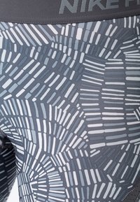 Nike legíny v šedobílém vzoru se liniovými tvary. Vyrobené z elastického materiálu s hladkou texturou a širokým pasem.