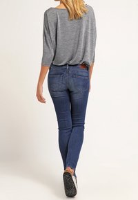 Top gris holgado con un escote ancho, combinado con jeans ajustados de color azul oscuro. El conjunto presenta un sutil desvanecimiento y bolsillos traseros.
