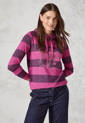 Rosa und dunkelviolette gestreifte Kapuzenjacke mit einer Kängurutasche, verstellbarem Kapuzenzug und Grafikdruck auf der Brust, kombiniert mit dunkelblauen Jeans.