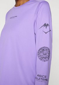 Πουκάμισο με μακριά μανίκια από ανοιχτό μ οβ ύφασμα. Φέρει γραφικό μαύρου βουνού σε ένα μανίκι και το λογότυπο ASICS FUJITRAIL στο μπροστινό μέρος. Ομαλή υφή.