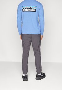 Ljust blå långärmad skjorta med svart "Patagonia"-logotyp på ryggen, kombinerad med grå byxor och svarta sneakers, sedd bakifrån.