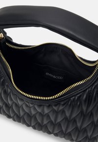 Sac à main matelassé noir avec fermeture éclair dorée partiellement ouverte, montrant l'intérieur en tissu noir et l'étiquette « even&odd » à l'intérieur.